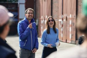 A man and a woman are talking to a group facing them.